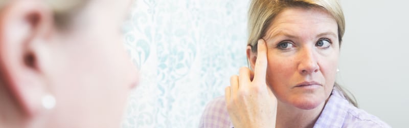 woman looking at her face in the mirror