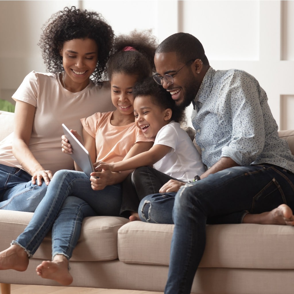 family on couch all looking into tablet device and smiling