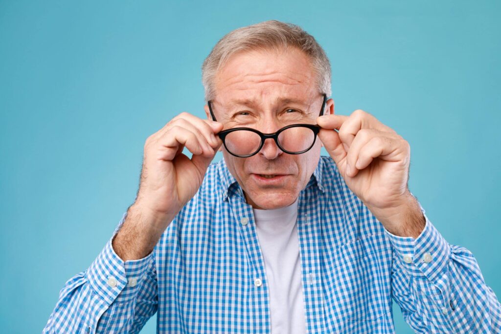 Early Signs of AMD You Shouldn’t Ignore 1 Older man holding up glasses struggling to see due to AMD symptoms in Chesapeake, VA