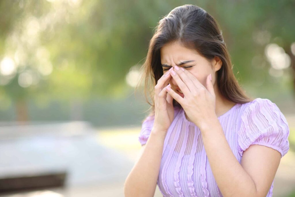 When to See an Eye Doctor for Allergic Conjunctivitis 1 Woman outside covering eyes in pain from allergic conjunctivitis symptoms in Chesapeake, VA